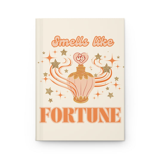 Journal with an illustration of a pastel orange vintage perfume bottle surrounded by glittery stars, and  'Smells like Fortune' text written in pastel orange retro aesthetic letters